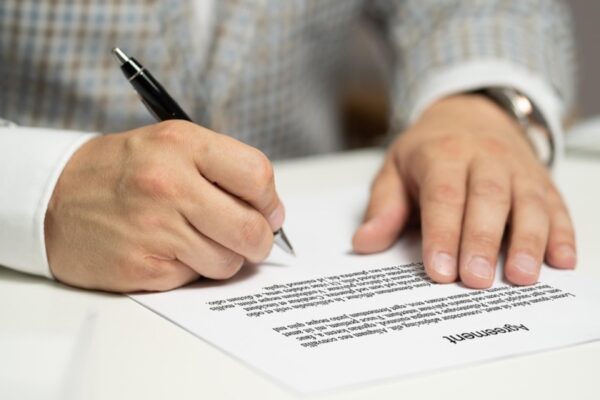 Manos firmando la documentación de una compraventa sobre una mesa de oficina